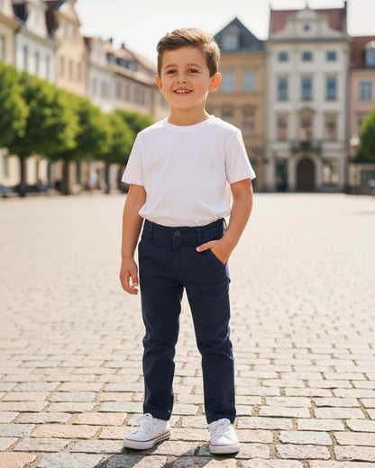 Young boy wearing Andy and Evan navy cotton pants and white t-shirt, standing on a cobblestone street.