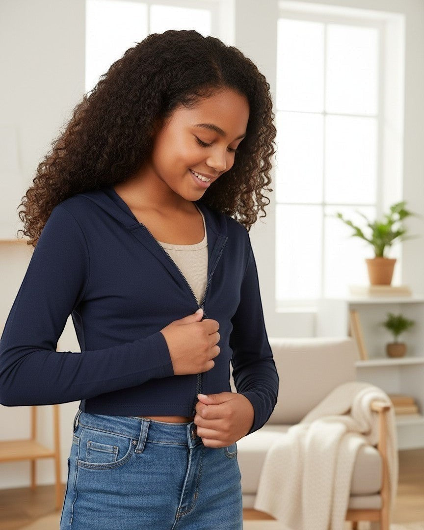 Model wearing a Calla Lily Cosmetics + CL kids navy French Terry crop zip-up hoodie with long sleeves in a bright room.
