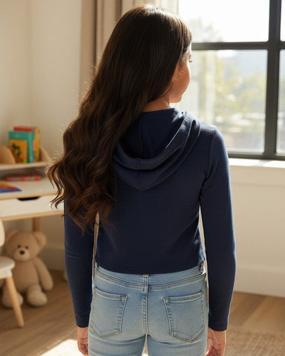 Model wearing a navy French Terry crop zip-up hoodie by Calla Lily Cosmetics + CL kids in a bright bedroom.