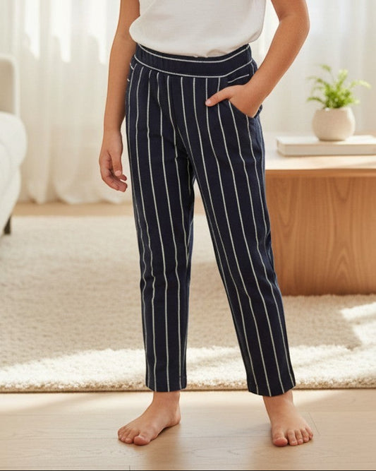 Girl wearing Calla Lily Cosmetics + CL kids navy pinstripe jersey pants with a white t-shirt in a bright living room.