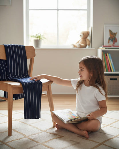 Calla Lily Cosmetics + CL kids navy pinstripe jersey pants draped on a chair next to a girl reading a book