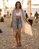 Model wearing a Calla Lily Cosmetics + CL kids olive viscose kimono cardigan with white print and tassels on a beach