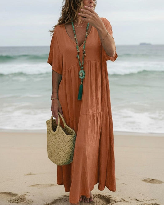 Woman wearing a Calla Lily Cosmetics + CL kids orange cotton tiered maxi dress on a beach with a straw bag.