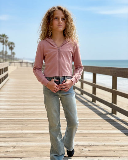 Model wearing a pink French Terry Crop Zip Up Hoodie by Calla Lily Cosmetics + CL kids on a sunny wooden boardwalk.