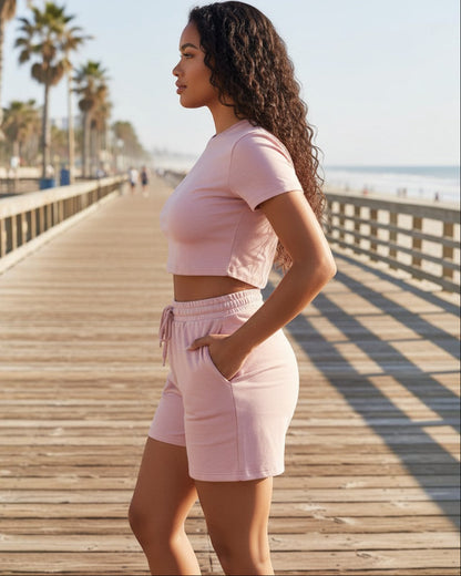 Model wearing Calla Lily Cosmetics + CL kids pink two-piece set with fitted crop tee and drawstring shorts on pier.