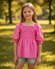 Girl wearing a pink puff sleeve top by Calla Lily Cosmetics + CL kids, featuring a smocked bodice in soft fleece.