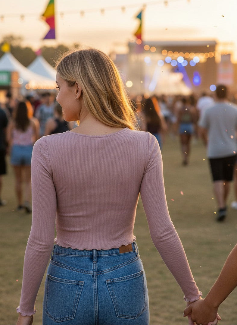 Woman wearing a Calla Lily Cosmetics + CL kids pink ribbed long sleeve top at an outdoor music festival at sunset.