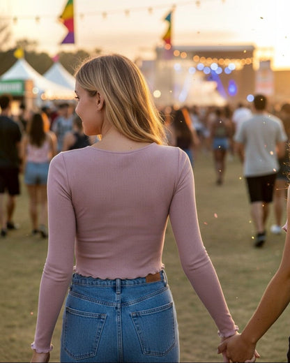 Woman wearing a Calla Lily Cosmetics + CL kids pink ribbed long sleeve top at an outdoor music festival at sunset.