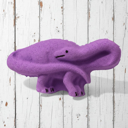 Calla Lily Cosmetics + CL kids purple brontosaurus dinosaur bath bomb with grape scent on a white wooden background.