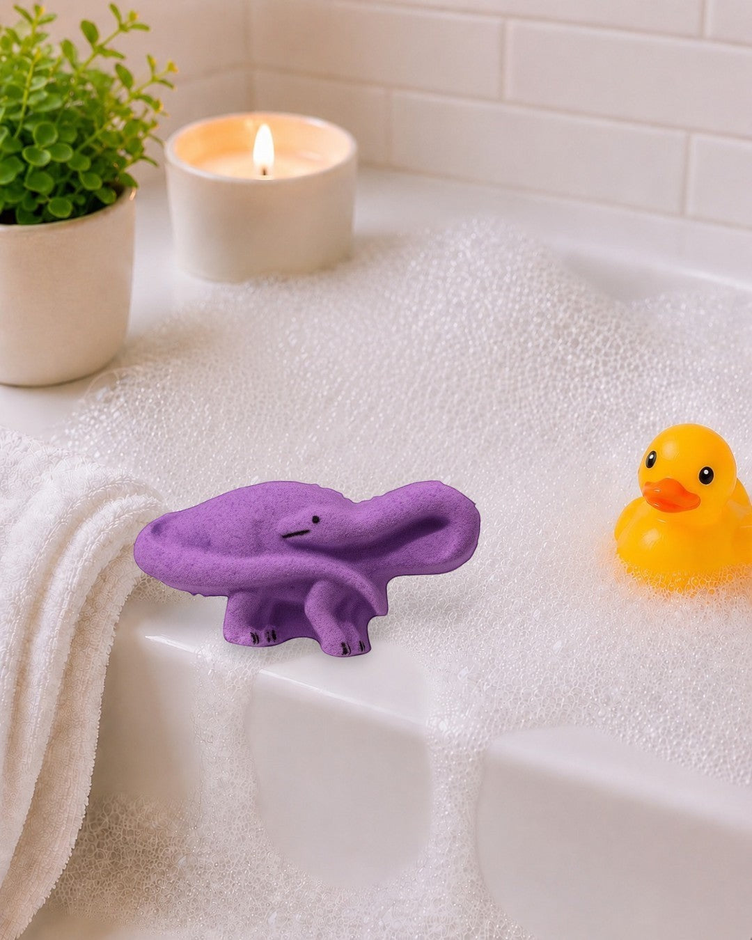 Calla Lily Cosmetics + CL kids purple brontosaurus dinosaur bath bomb with grape scent on a white wooden background.