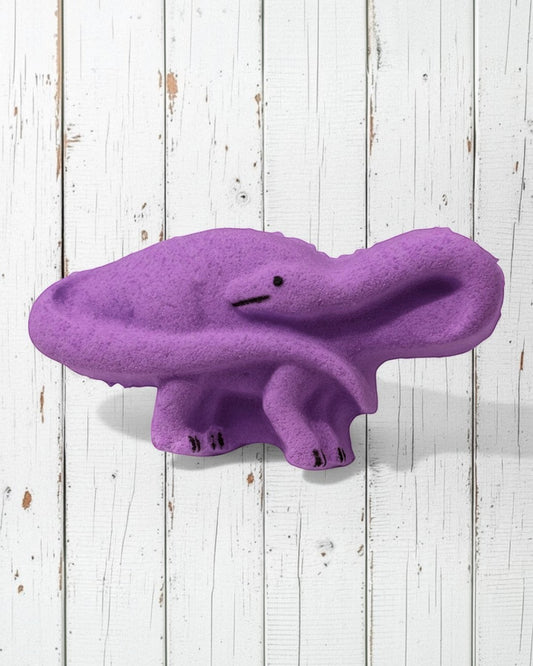 Calla Lily Cosmetics + CL kids purple brontosaurus dinosaur bath bomb with grape scent on a white wooden background.