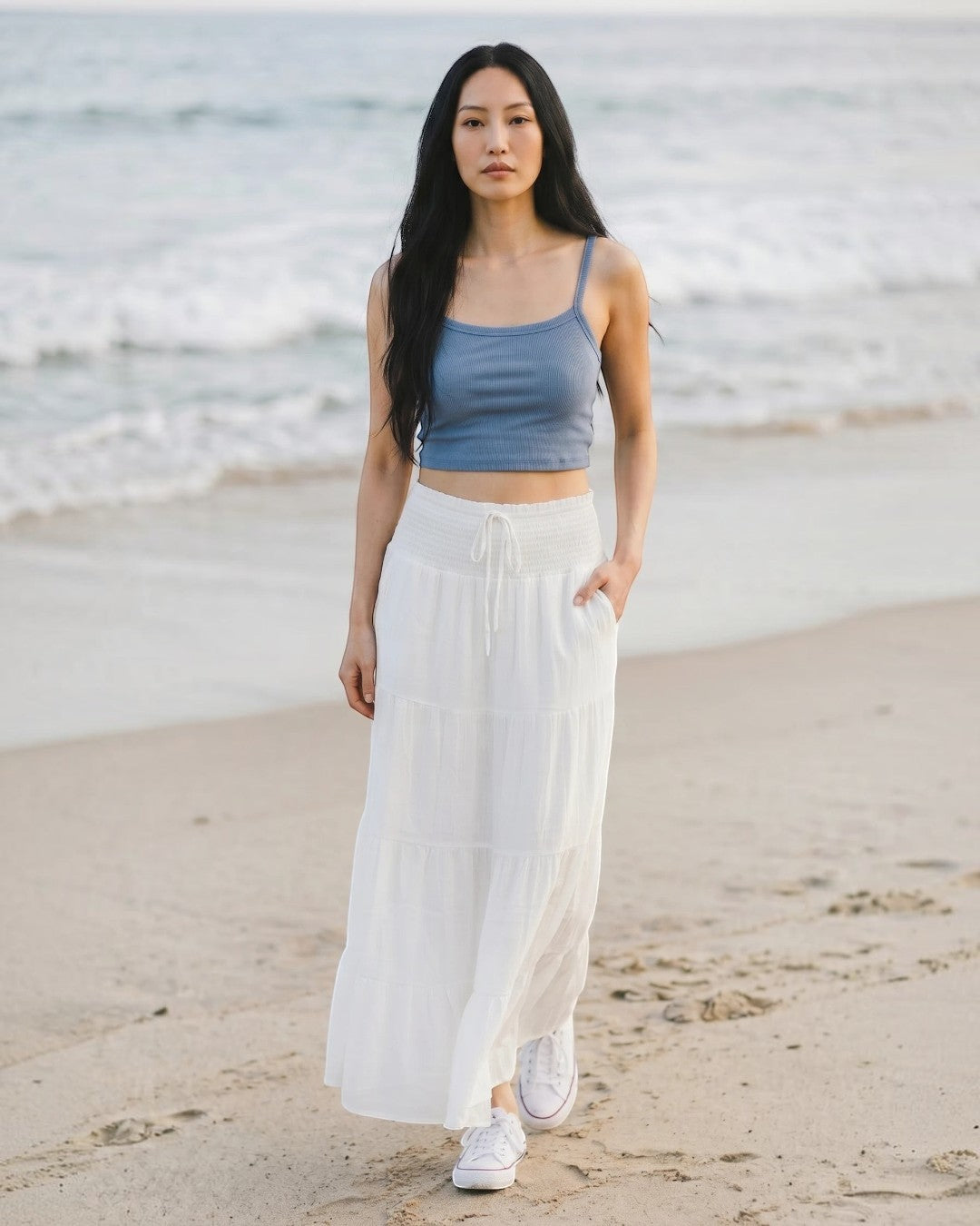 Model wearing Calla Lily Cosmetics + CL kids blue ribbed knit crop tank top with a white tiered maxi skirt on a beach.