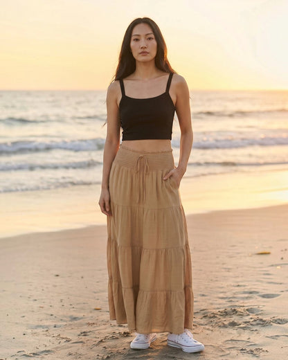 Model wearing Calla Lily Cosmetics + CL kids black ribbed knit crop tank top with a tan tiered maxi skirt at sunset.