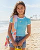 Girl wearing a Calla Lily Cosmetics + CL kids blue ribbed crew neck top with lemon embroidery on a sunny beach.