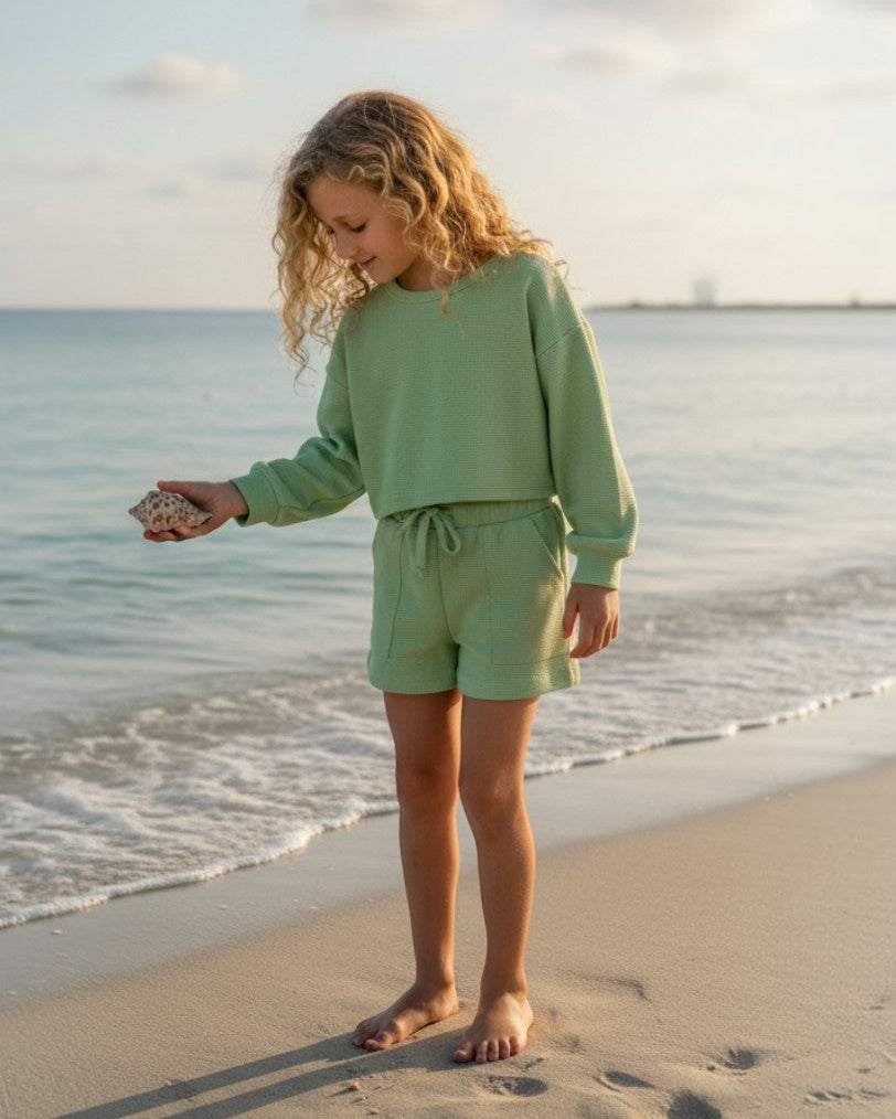 Girl wearing Calla Lily Cosmetics + CL kids sage green waffle knit long sleeve shirt and shorts set on the beach.