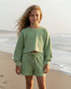 Tween girl wearing a sage waffle knit two-piece set from Calla Lily Cosmetics + CL kids on a beach at sunset.