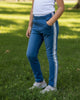 Child wearing Calla Lily Cosmetics + CL kids blue skinny jeans with side stripes and white tank top in a park.