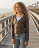 Model wearing a taupe Calla Lily Cosmetics + CL kids French Terry crop zip-up hoodie on a beach boardwalk.