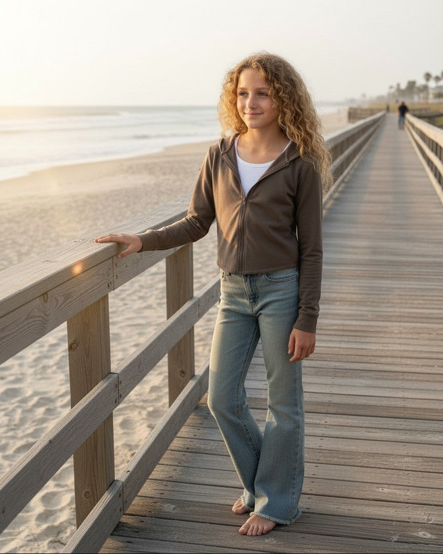 Model wearing a Calla Lily Cosmetics + CL kids taupe French Terry crop zip-up hoodie on a wooden beach pier.