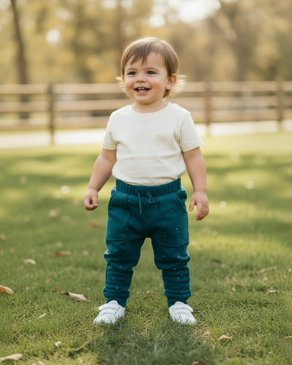 Toddler wearing Calla Lily Cosmetics + CL kids teal cotton joggers with white specs in a grassy park.