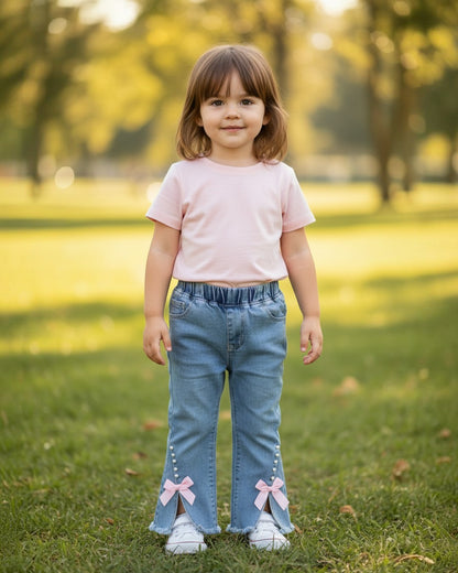 Toddler wearing Calla Lily Cosmetics + CL kids blue jeans with raw hem, pearl accents, and pink bows in a park.