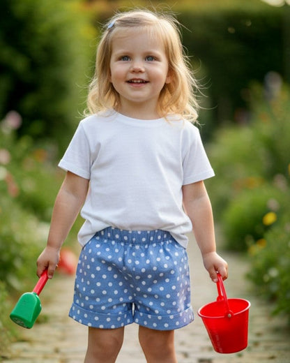 Toddler wearing Calla Lily Cosmetics + CL kids blue polka dot cotton shorts with elastic waist and pockets in a garden