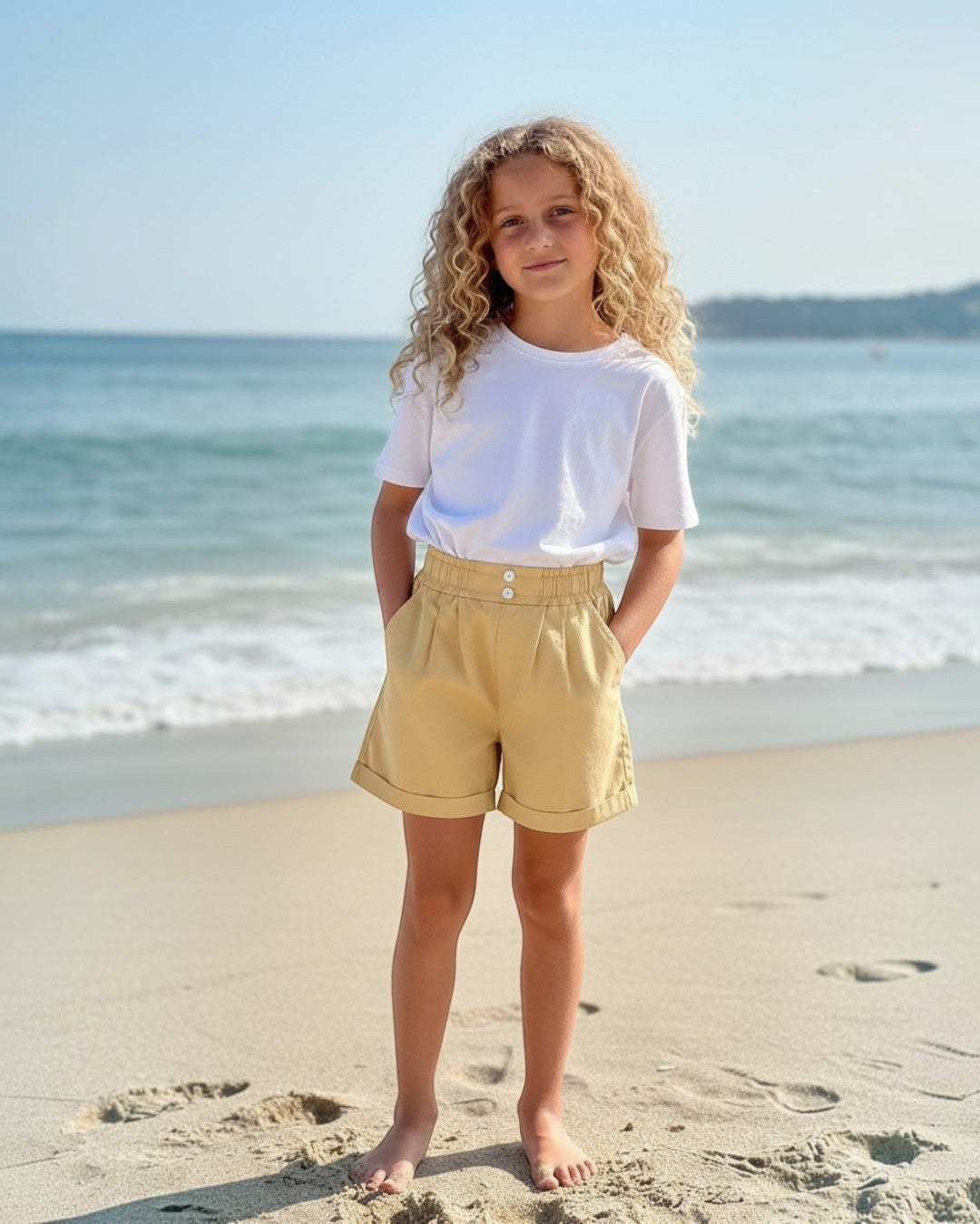 Girl wearing Calla Lily Cosmetics + CL kids yellow cotton shorts with a ruffled waistband on a sunny beach.