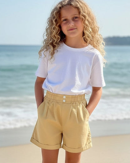 Girl wearing Calla Lily Cosmetics + CL kids yellow cotton shorts with a ruffled waistband on a sunny beach.