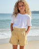 Girl wearing Calla Lily Cosmetics + CL kids yellow cotton shorts with a ruffled waistband on a sunny beach.