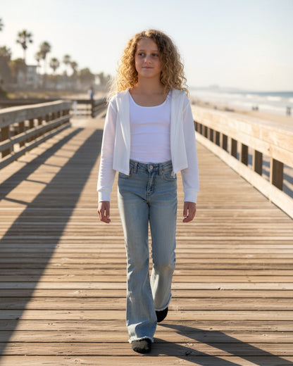 Girl with curly hair wearing a white Calla Lily Cosmetics + CL kids French terry crop zip-up hoodie on a pier.