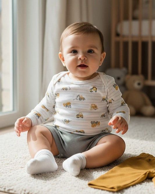 Calla Lily Cosmetics + CL kids 4-piece baby jumper set with white long-sleeve bodysuit featuring construction trucks and grey shorts and mustard yellow pants.