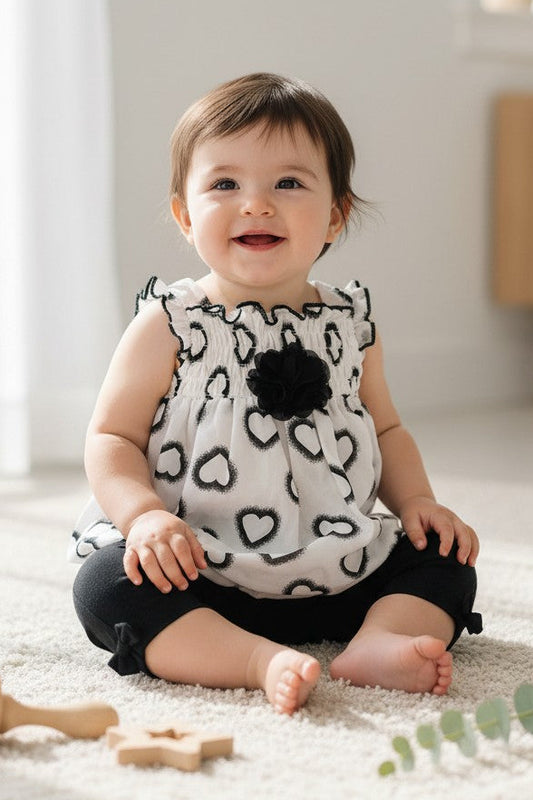 Calla Lily Cosmetics + CL kids white chiffon baby top with black hearts and flower accent, paired with black leggings with bows. 100% polyester.