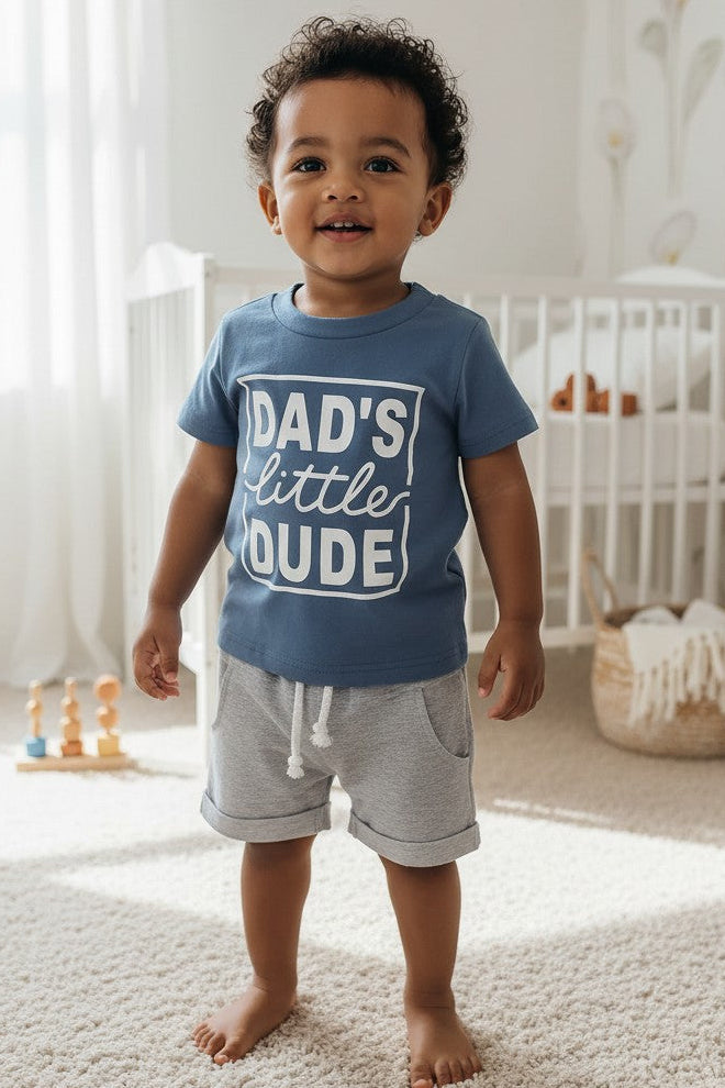 Calla Lily Cosmetics + CL kids blue graphic tee with "DAD'S little DUDE" text and grey shorts with drawstring. Cotton-polyester blend.