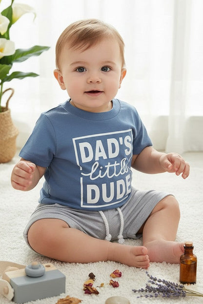 Calla Lily Cosmetics + CL kids blue graphic tee with "DAD'S little DUDE" text and grey shorts with drawstring. Cotton-polyester blend.