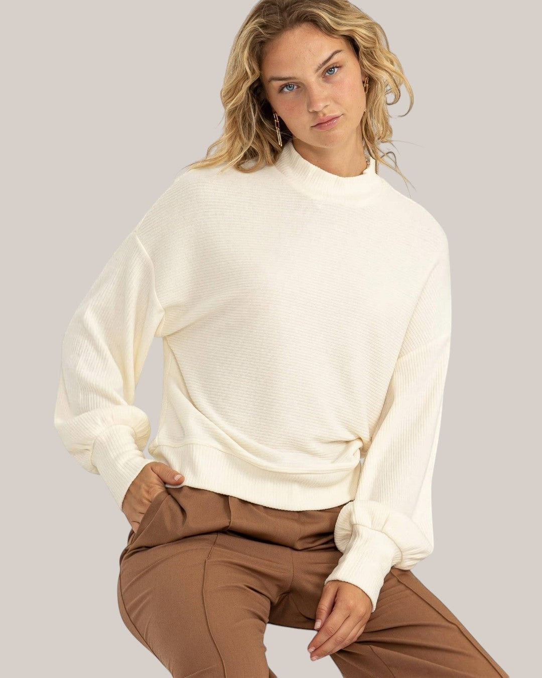 Calla Lily Cosmetics + CL kids cream ribbed balloon sleeve pullover worn by a model with brown trousers