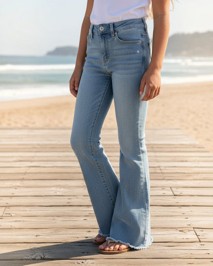 Calla Lily Cosmetics + CL kids girls light wash stretchy denim flare jeans with a frayed hem on a beach boardwalk.