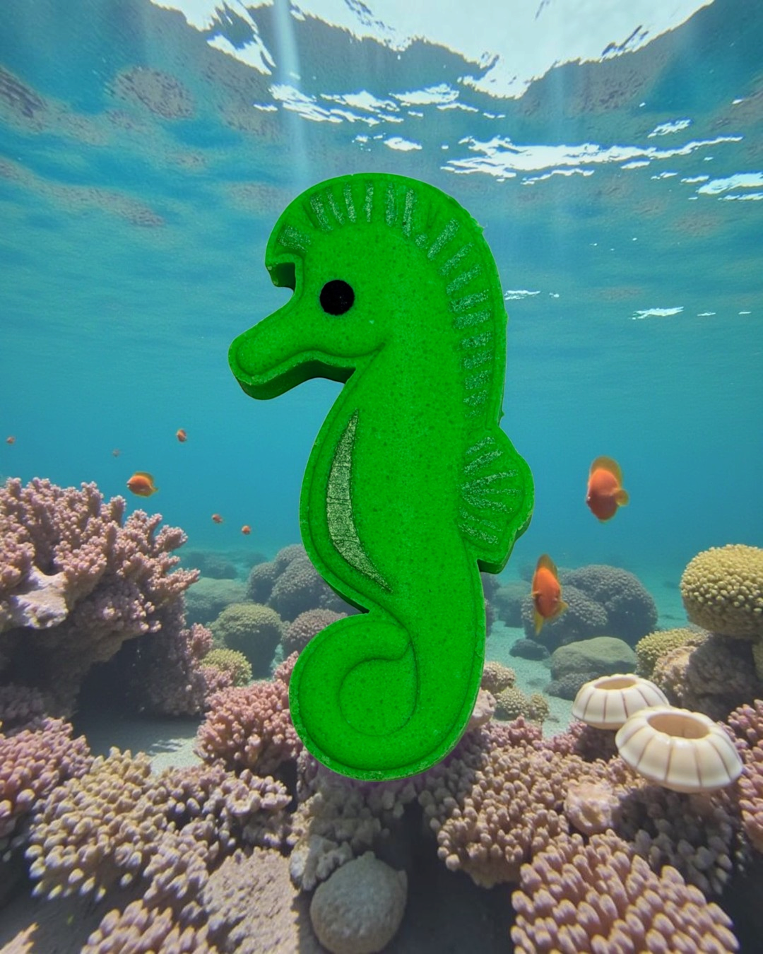 Calla Lily Cosmetics + CL kids green seahorse-shaped bath bomb floating in a vibrant underwater coral reef scene