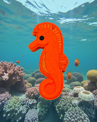 Calla Lily Cosmetics + CL kids orange seahorse shaped bath bomb floating against an underwater coral reef background