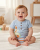 Calla Lily Cosmetics + CL kids light blue organic cotton baby bodysuit with giraffe in safari jeep graphic and striped trim. Wooden buttons.