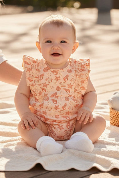 Calla Lily Cosmetics + CL kids peach cotton romper with seashell and starfish print, ruffled sleeves, and snap closures.