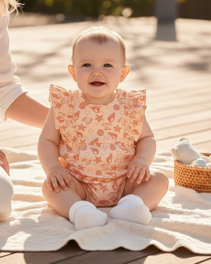Calla Lily Cosmetics + CL kids peach cotton romper with seashell and starfish print, ruffled sleeves, and snap closures.
