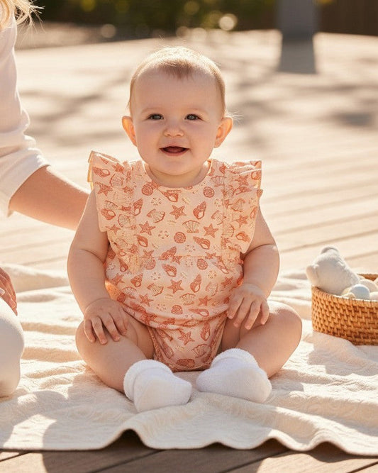 Calla Lily Cosmetics + CL kids peach cotton romper with seashell and starfish print, ruffled sleeves, and snap closures.