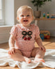 Calla Lily Cosmetics + CL kids pink cotton bodysuit with black polka dots, ruffled collar, and cherry bow applique. Lap shoulders and snap closure.