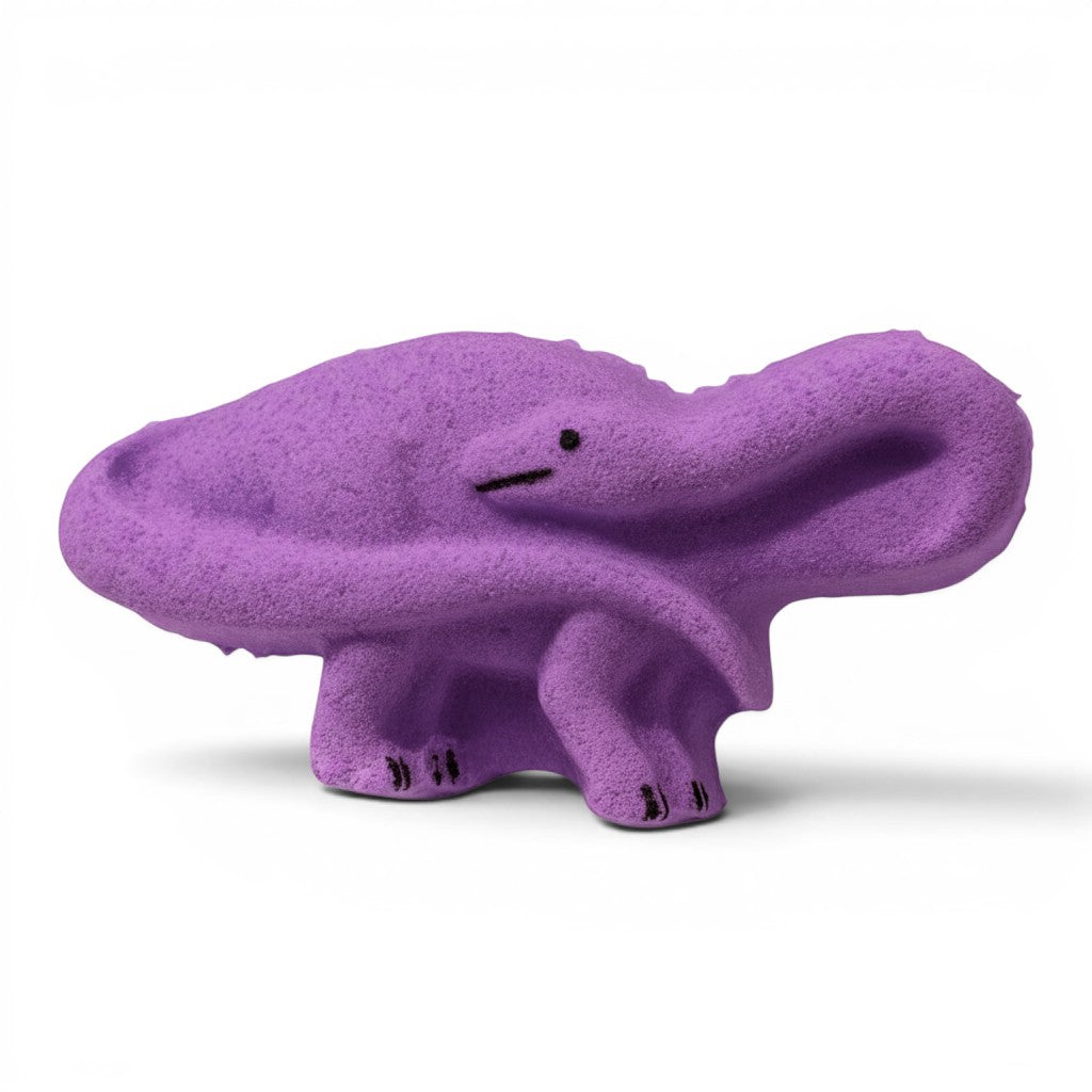 Calla Lily Cosmetics + CL kids purple brontosaurus dinosaur bath bomb with grape scent on a white wood background.