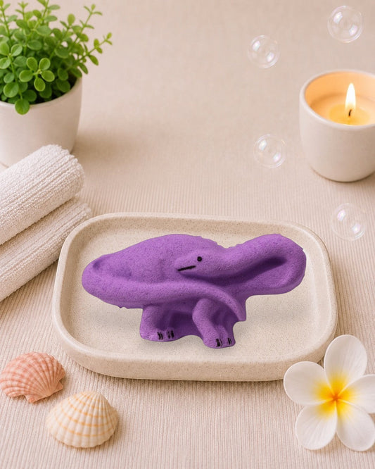 Calla Lily Cosmetics + CL kids purple brontosaurus dinosaur bath bomb with grape scent on a white wood background.