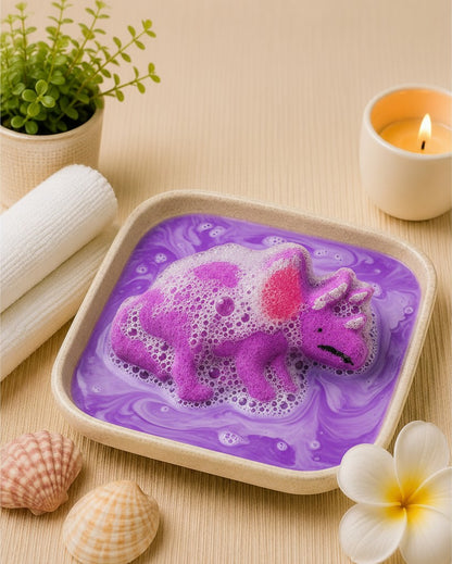 Calla Lily Cosmetics + CL kids purple Triceratops dinosaur bath bomb fizzing in a square bowl of grape-scented water.