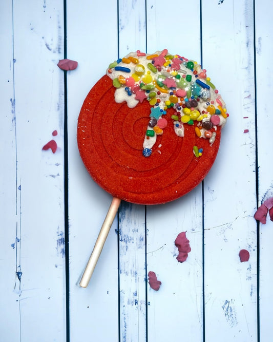 Calla Lily Cosmetics + CL kids red orange lollipop bath bomb with colorful sprinkles on a rustic white wood background