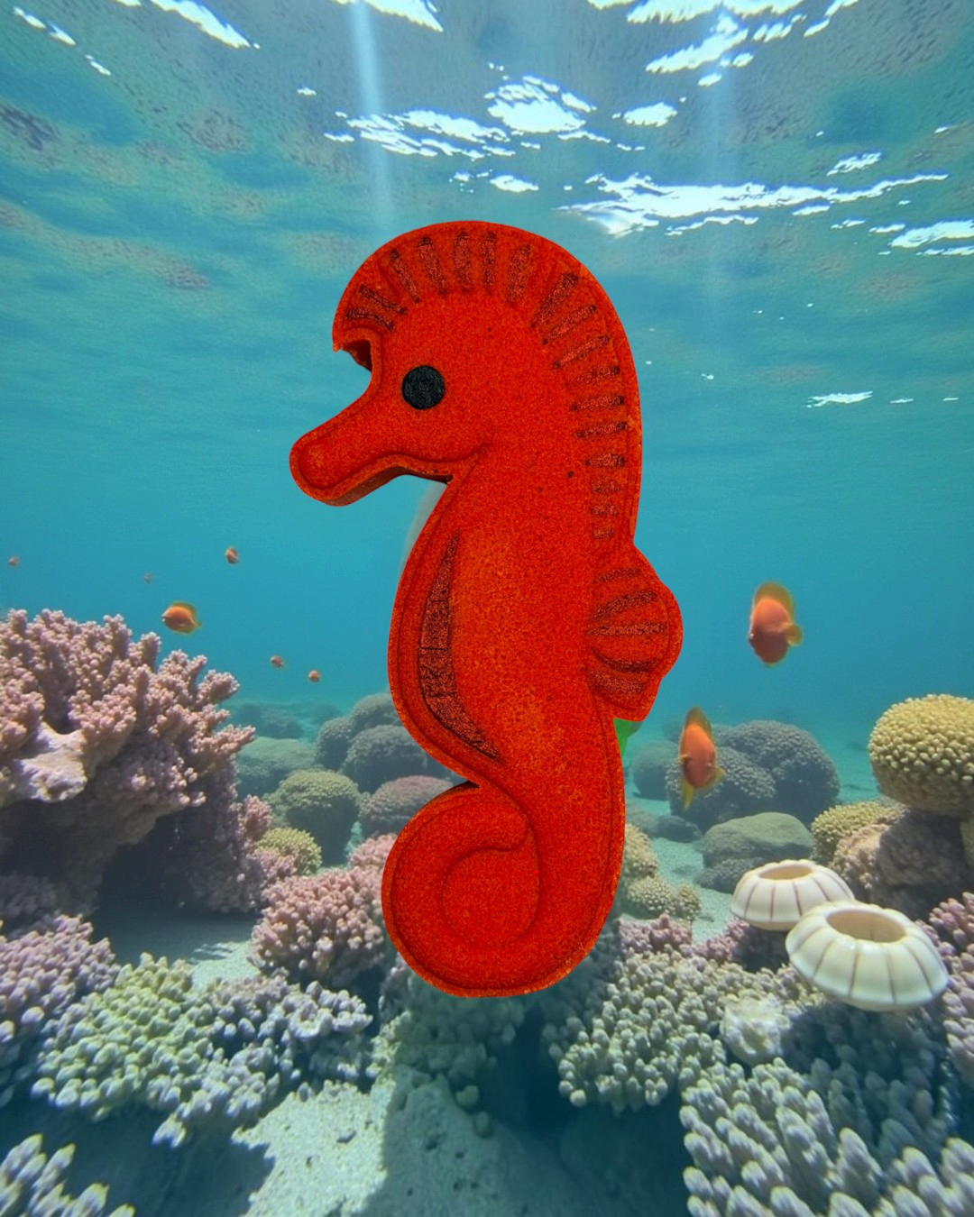 Calla Lily Cosmetics + CL kids red seahorse bath bomb with blood orange scent against an underwater coral reef backdrop