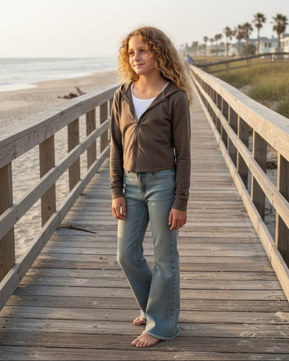 Calla Lily Cosmetics + CL kids taupe French Terry crop zip-up hoodie worn by a girl on a wooden beach boardwalk.