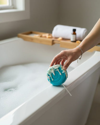 Calla Lily Cosmetics + CL kids teal lollipop bath bomb with white icing and sprinkles held over a bubbly bathtub